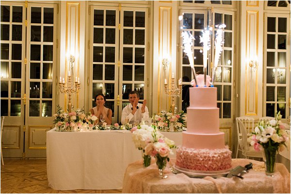 Bride and groom enjoy sparklers on pastel pink cake