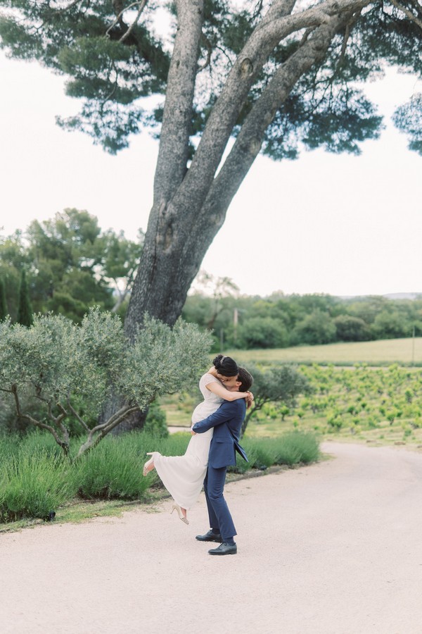 Groom lifts bride up into embrace underneath tree