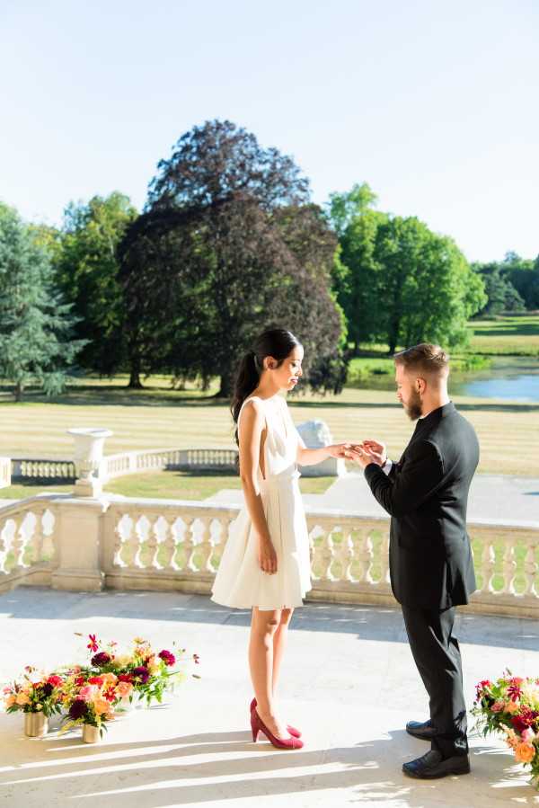 Groom puts ring on Brides finger in front of English Garden