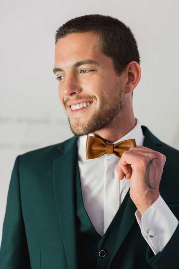 Groom in bottle green suit and brown leather bow tie