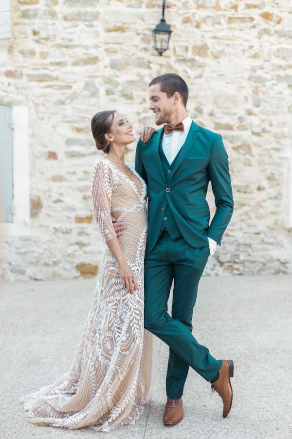 Bride in gown and groom in green suit pose lovingly