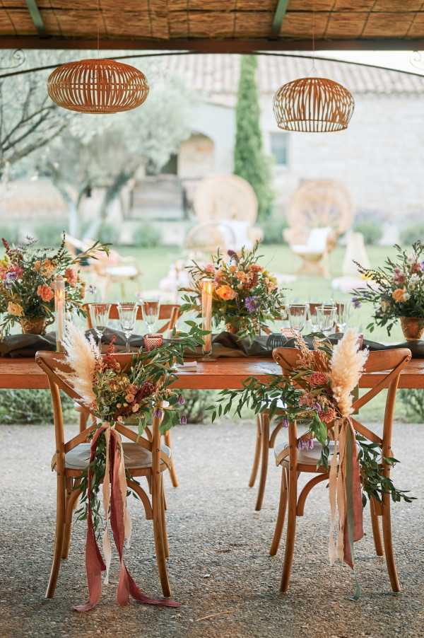 Floral arrangements tied with ribbon to the back of bridal chairs of rustic wood