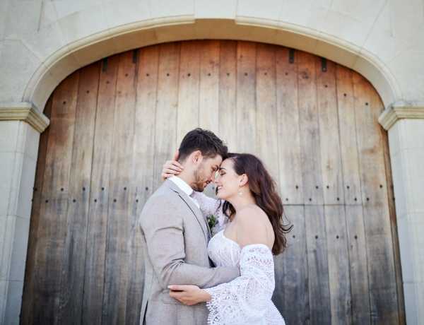 Bride and groom embrace in front of rustic wooden arch way