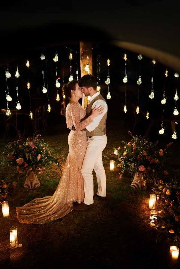 Bride and groom kiss in the dark of night under festoon lighting