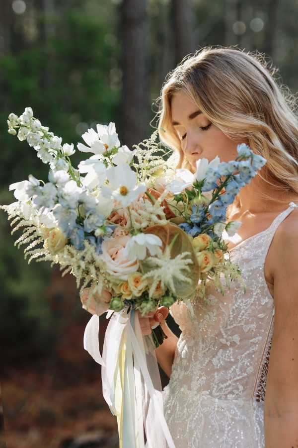 Dappled sunlit bride closes eyes and smells bouquet