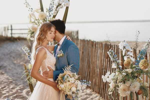 Couple kiss at beach wedding in afternoon sun groom in blue suit