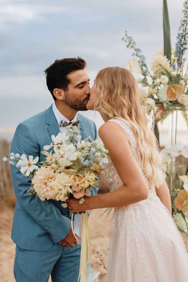 Couple in natural colours and blues kiss in beachside wedding in France