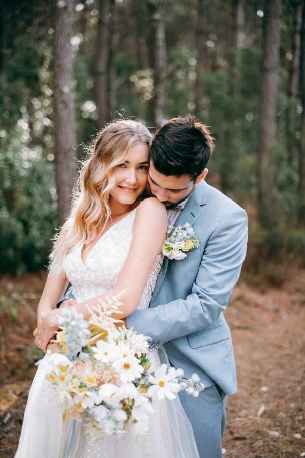 Bride and groom hug in forest wedding with ocean blue themed bouquet and suit