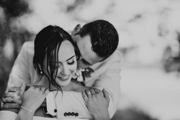 black and white image of groom with arms around brides neck from behind she is smiling