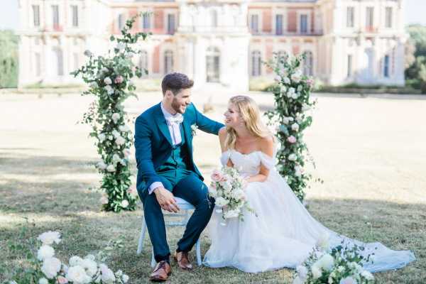 Couple seated by white rose arbor outside Chateau de Baronville France