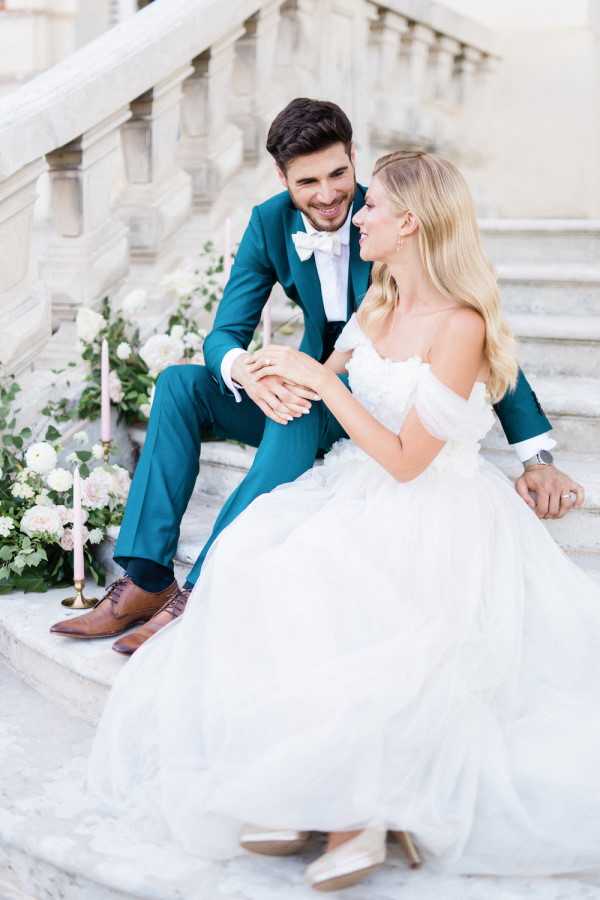 Bride and groom book lovers seated on stairs after literary themed wedding at Chateau de Baronville, France