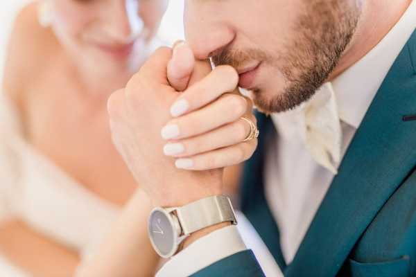 Close-up of groom in watch kissing brides hand 