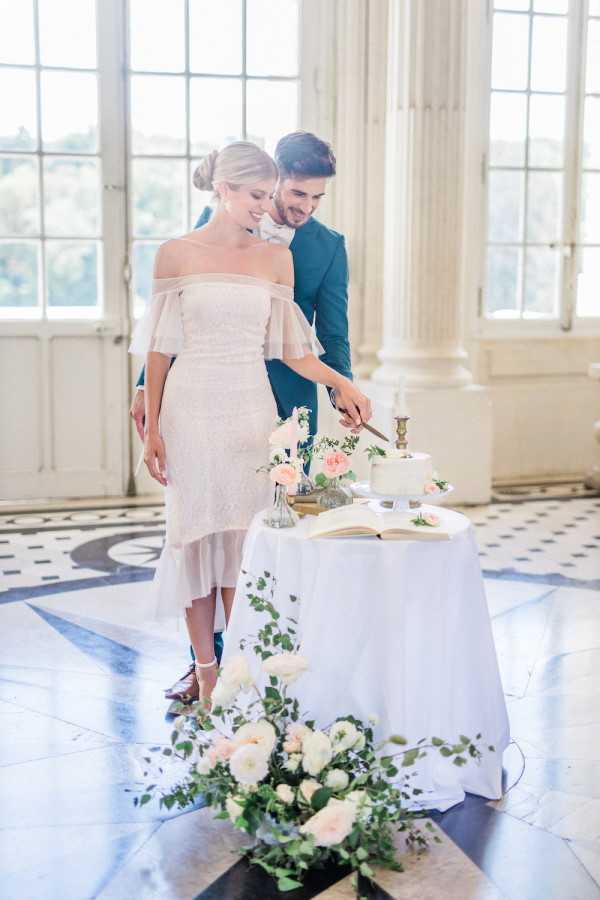 Bride and groom cut cake and stand together by windows in Chateau de Baronville France