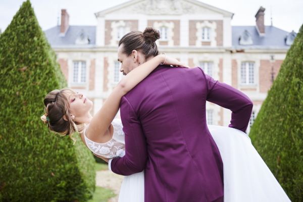 Groom in purple suit tips his bride back in front of Chateau Le Buisson Garembourg in France