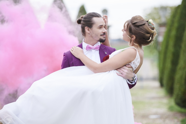 groom carries bride while pink smoke blooms behind them