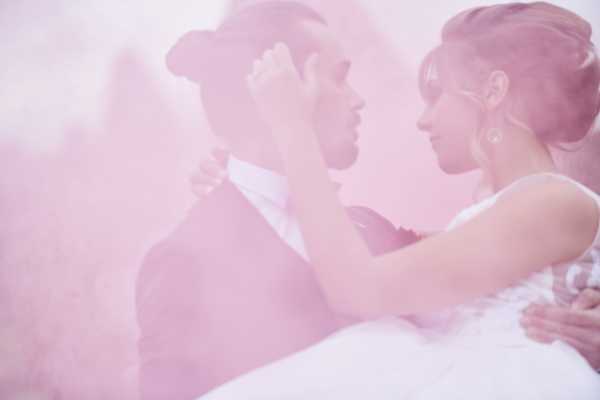 bride and groom just visible in each others arms through pink smoke haze