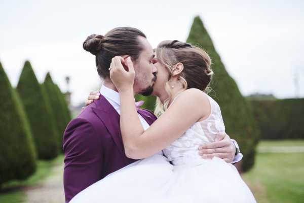 groom holds bride in his arms in manicured garden as they kiss each other