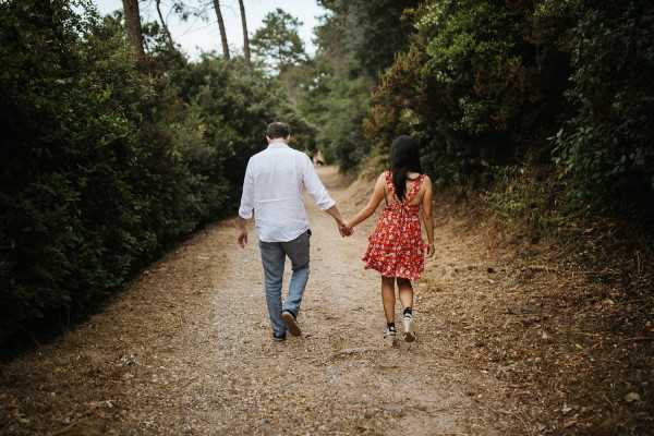 Couple walk hand in hand down gravel path with back to camera