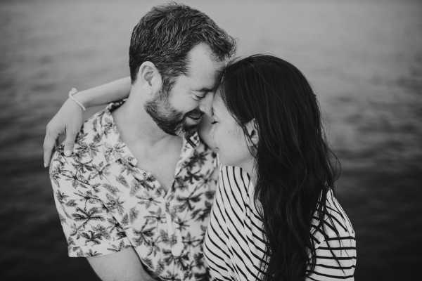 Black and white image of couple touch heads in warm embrace in floral and striped shirts