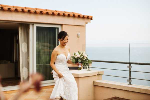 Bride approaches groom before wedding on balcony of hotel in white gown