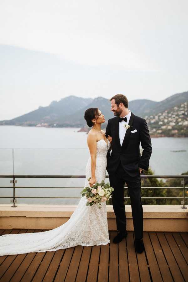 Bride and groom pose for photo in wedding outfits on balcony of hotel looking at each other