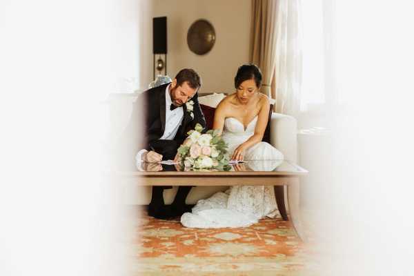 Bride and groom are photographed through door frame signing their wedding paperwork