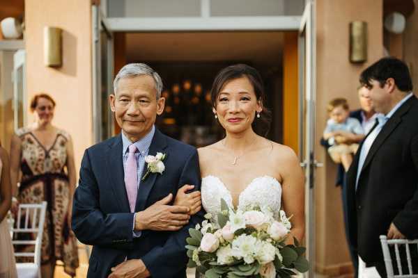 Bride walks down aisle on the arm of her father she wears a white strapless gown