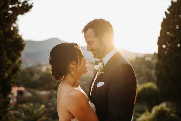 Mid-shot of bride and groom looking into each others eyes with sun shining through behind them