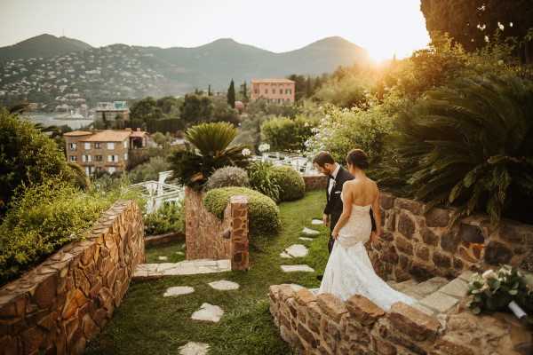 Bride in trailing dress and groom descend stairs into garden of hotel in France