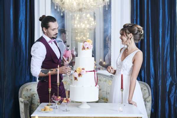 bride and groom cut cake with blue curtains behind them