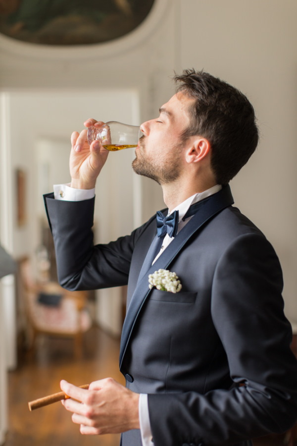 Groom sips whiskey before wedding ceremony in tuxedo