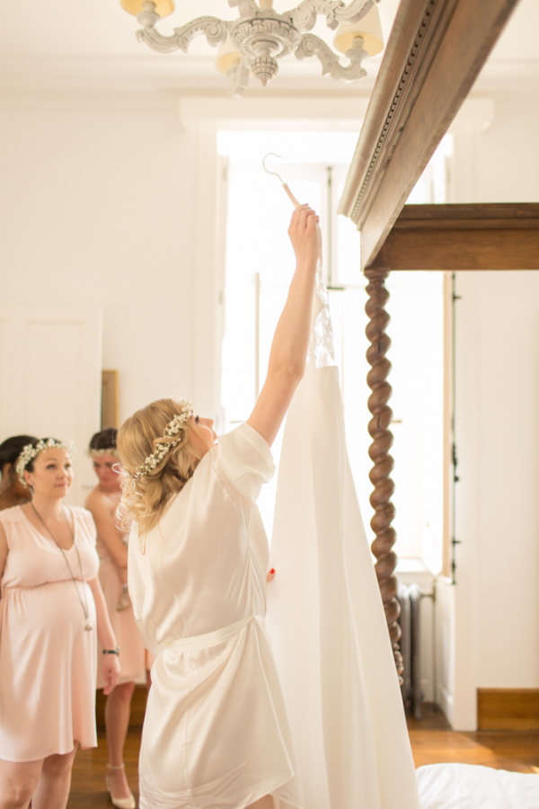 Bride reaches up to take wedding dress off hanger surrounded by bridesmaids