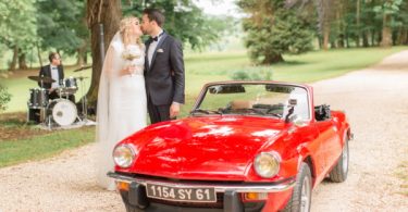 Bride and Groom kiss next to red convertible car at their Wedding at Chateau d'Azy