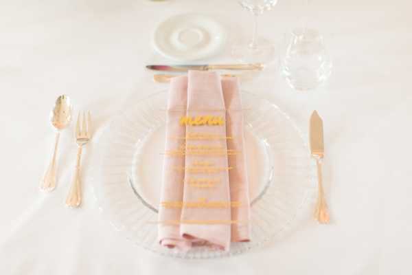 Table setting with pink napkin and clear and gold menu for wedding at Chateau d'Azy