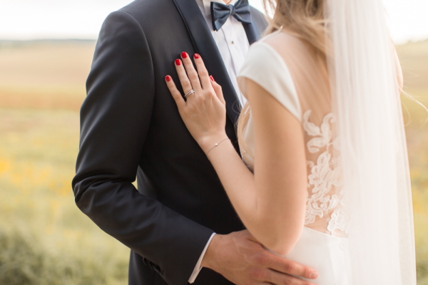 Bride with red manicure rests her hand on grooms chest in tuxedo