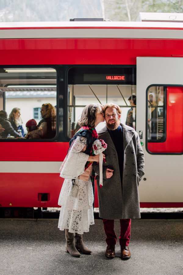 Bride and Groom kiss in front of red and white train on way to wedding