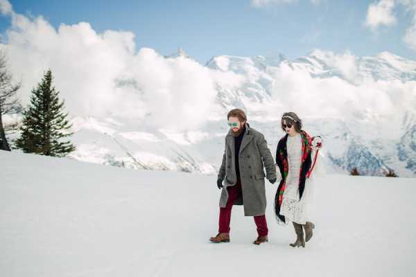 Bride and groom walk through the snow in boots in the French Alps in their suit and wedding dress