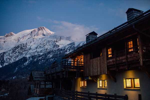 French Alps chalet in dark evening with lights and snow capped mountain in background