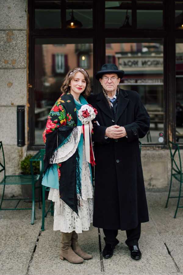 Bride in white lace dress with shawl and boots and bride's father in black woollen coat and top hat outside Brasserie and Bar