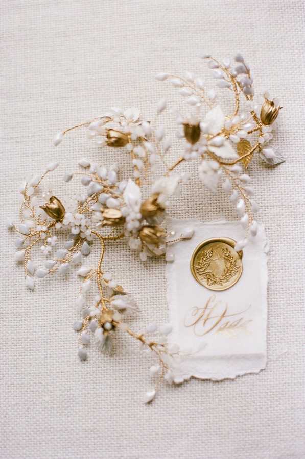 flat lay of gold and white floral hairpiece and gold wax seal on torn paper