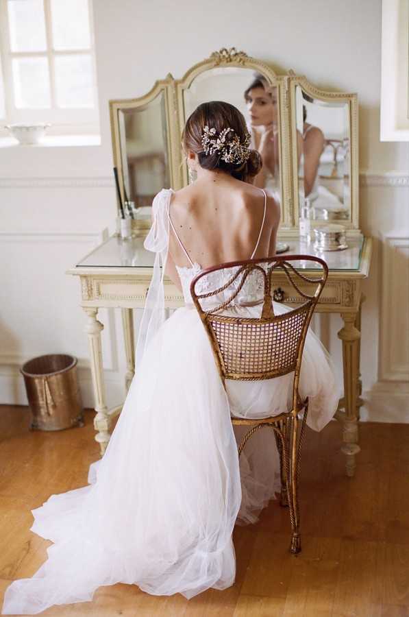 back of bride putting her earrings on in mirror of dressing table