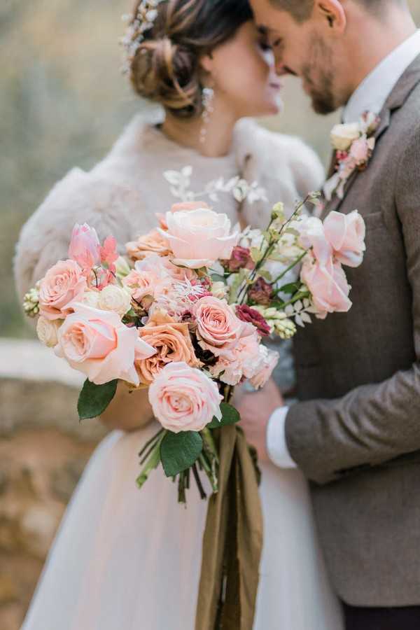 bride and groom kiss and hold pink bouquet close to camera