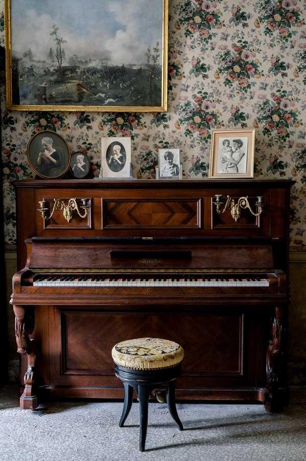 Dark wood piano and floral upholstered piano stool with black and white photo frames