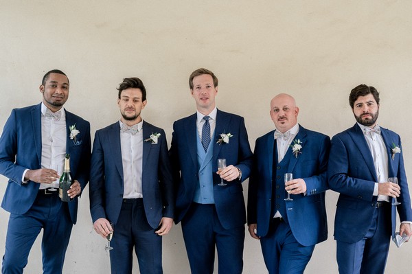 Groom and four groomsmen in blue suits holding champagne glasses