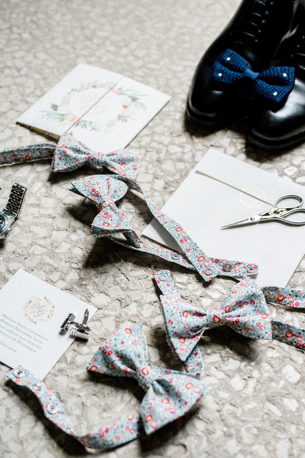 Flat lay of groom shoes, blue bow tie and floral bow ties for grooms men