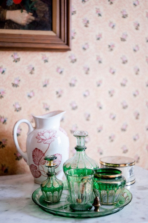 Crystal glassware on plate with ceramic jug in front of floral wallpapered wall