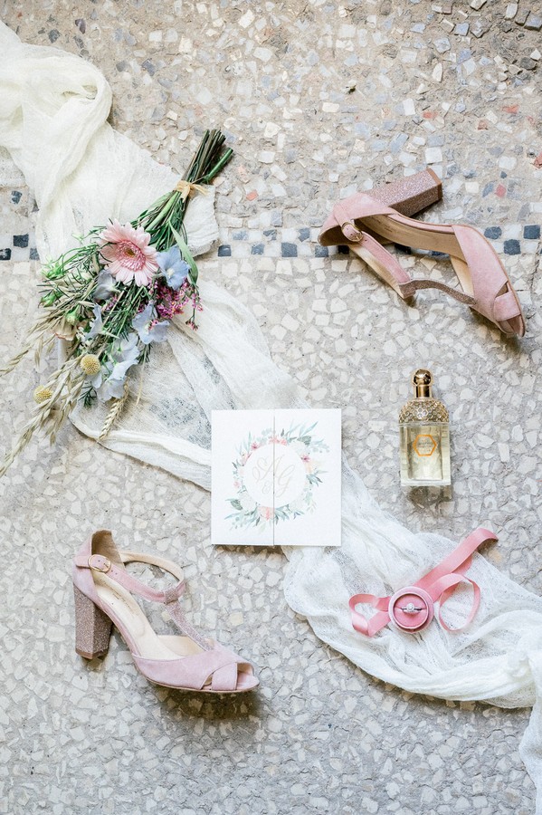 Flat lay of pink bridal shoes, pastel bouquet, floral wedding stationery and perfume