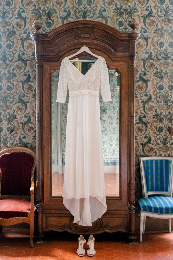 Wedding Dress hanging on the front of mirrored armoire in french wallpapered room