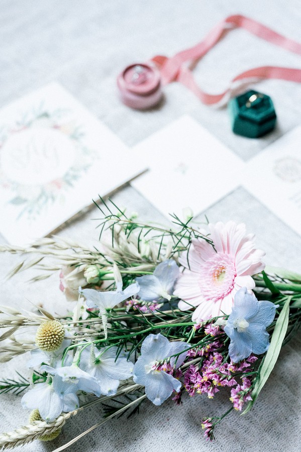 Flat lay of bouquet, pink and green ring boxes and floral stationery