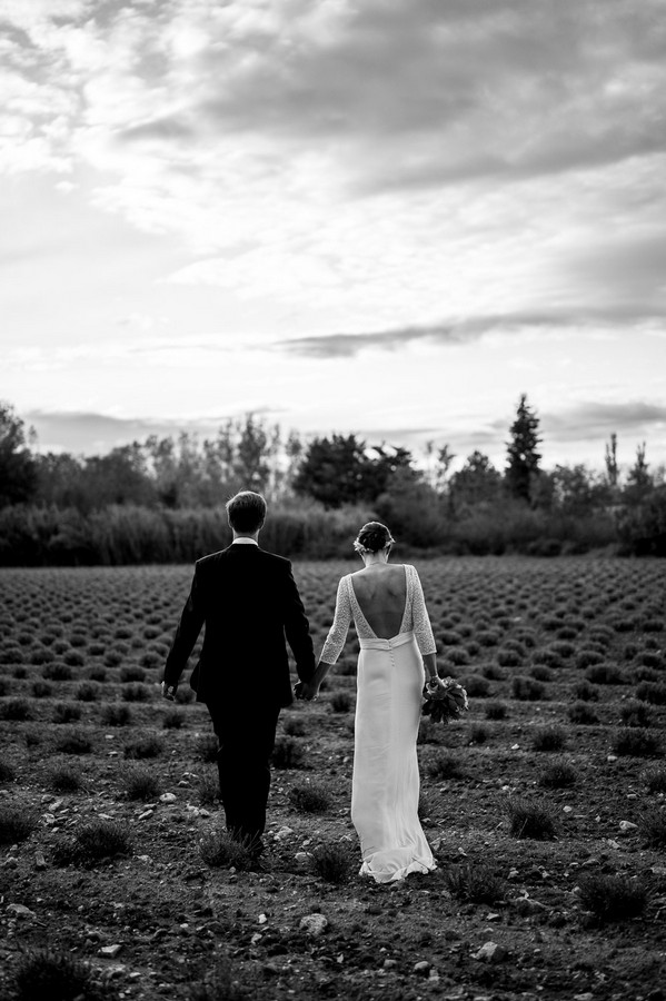 Black and white image of bride and groom walking away from camera through field